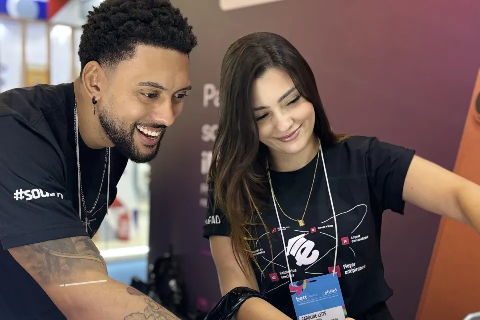 Dois integrantes do time da EAD Plataforma apresentando a plataforma em um notebook no estande da Bett Brasil