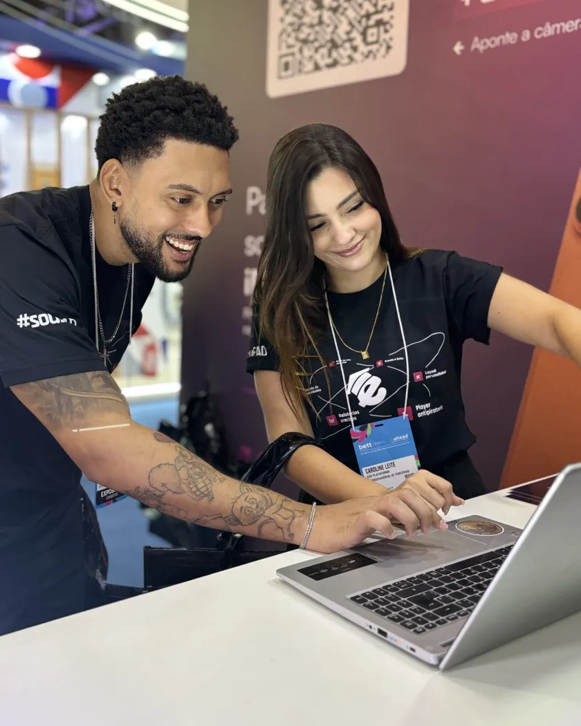 Dois integrantes do time da EAD Plataforma mostrando a plataforma em um notebook no estande da Bett Brasil